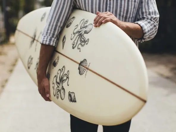 Enter to Win a FREE Custom Almond Surfboard with Your Design, hands holding personalized artwork on surfboard
