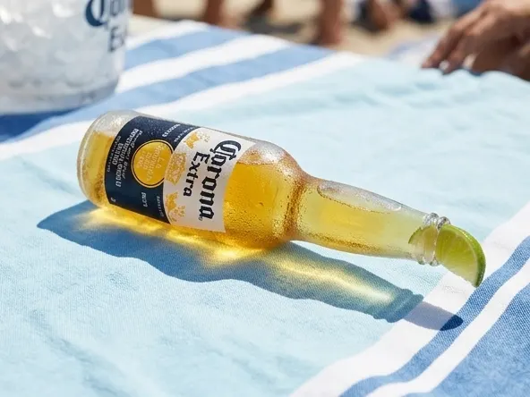 Enter Daily for FREE $200 Gift Cards or Corona Holiday Decor, chilled bottle resting on beach towel